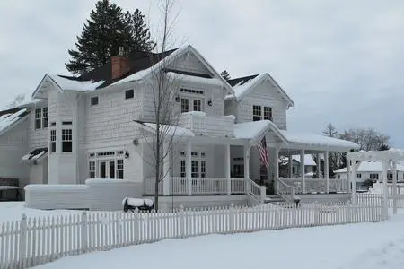 A white house with snow on the ground and trees in front of it.